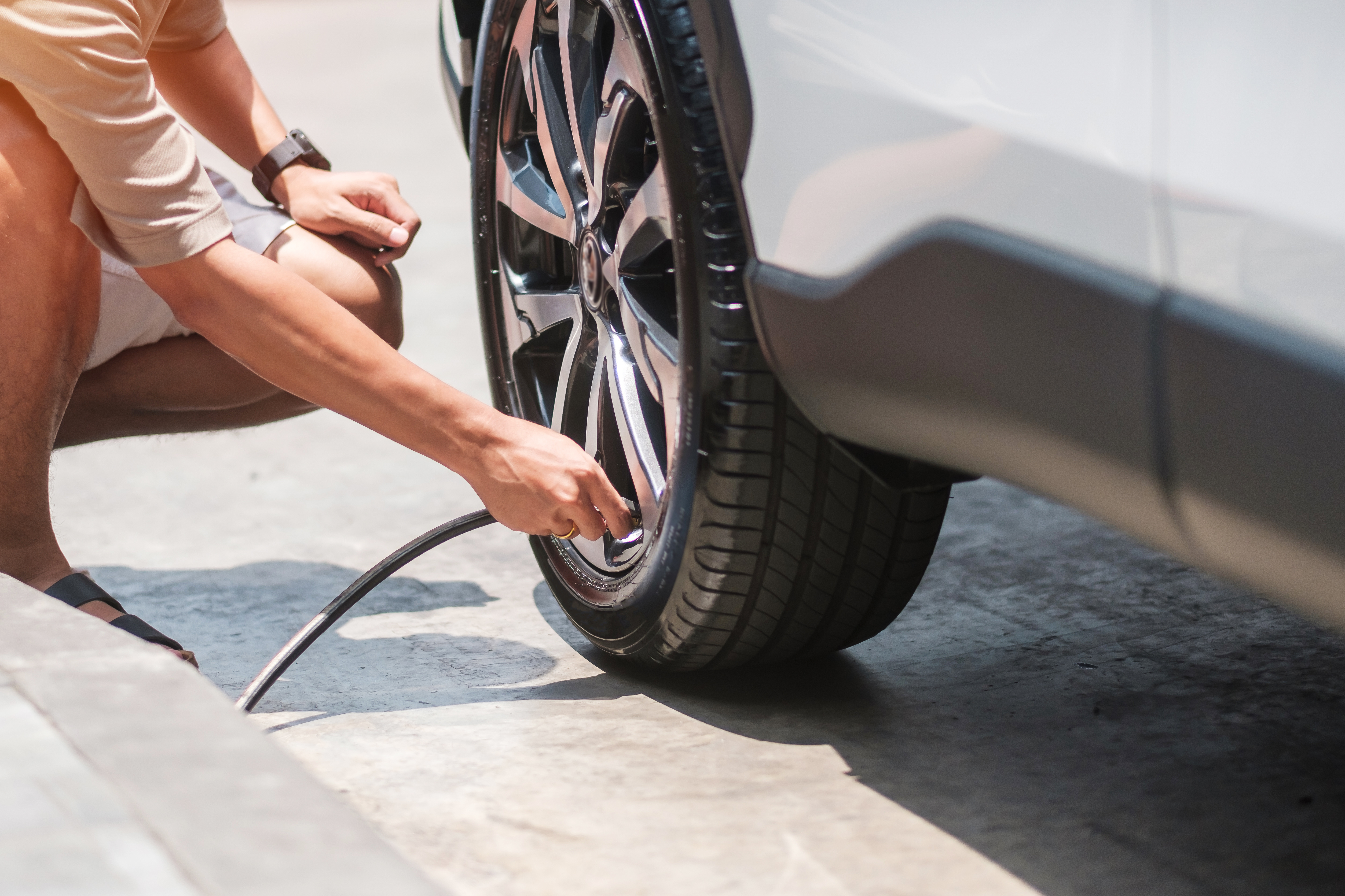 A man airing up his leaking car tire again using his tire's valve stem.