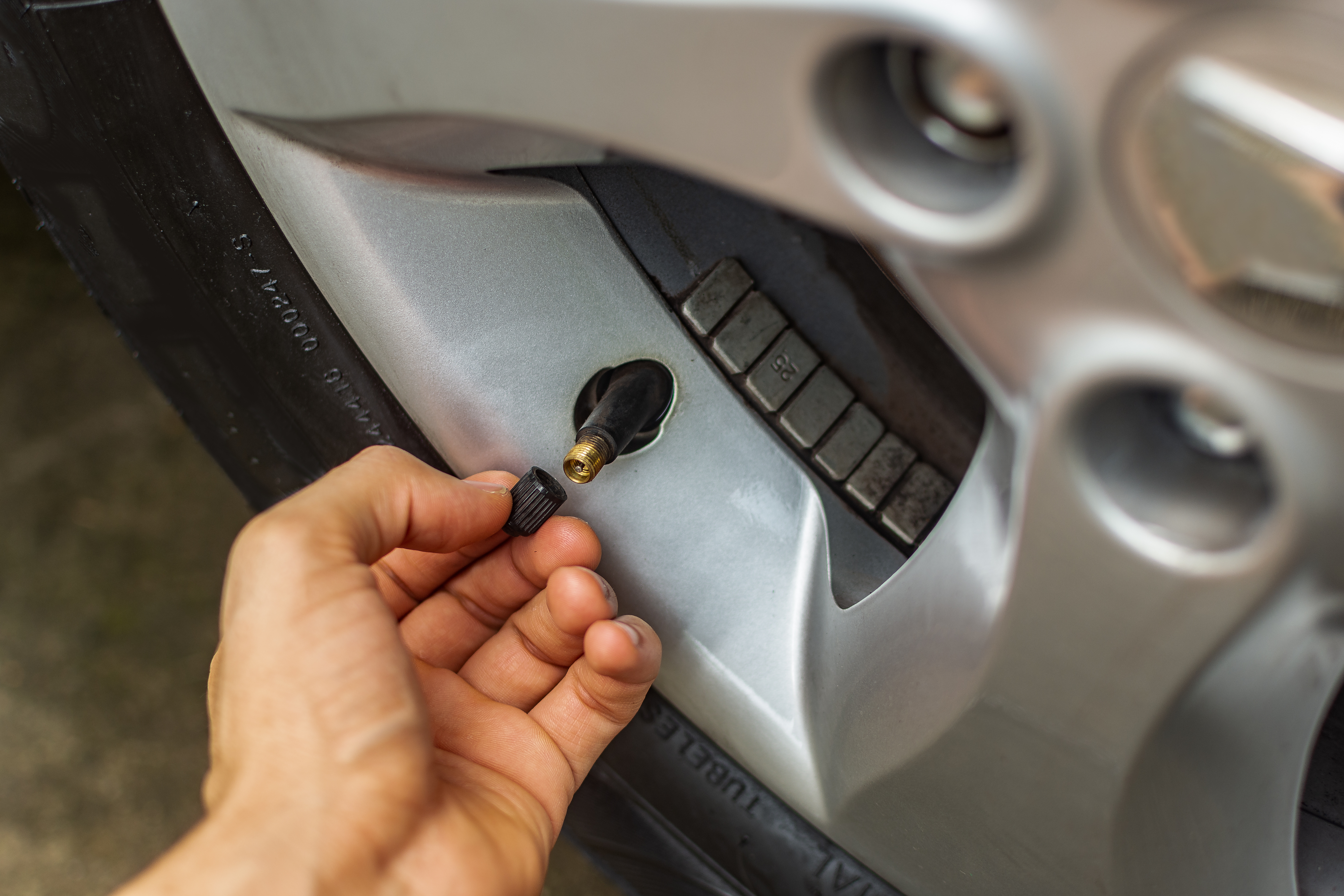 A man replacing his tire's valve cap after checking his valve stem for a slow leak.