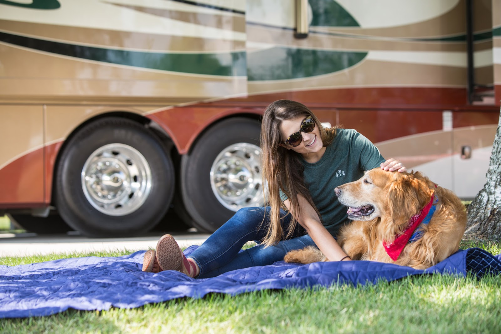 A woman sitting in the grass with her dog outside of her RV while camping.
