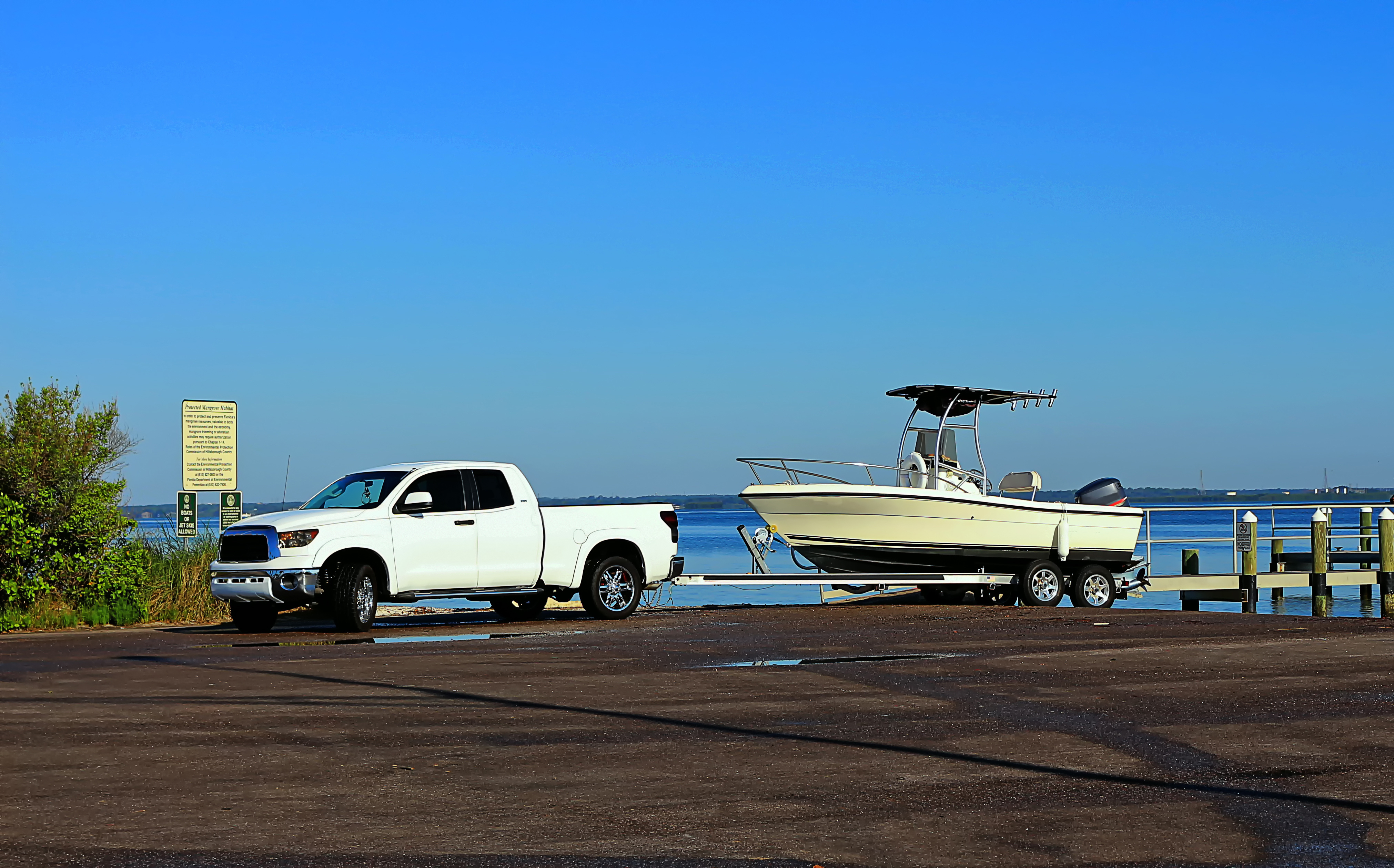 A white passenger truck is parked near the boat loading dock with a boat in tow.
